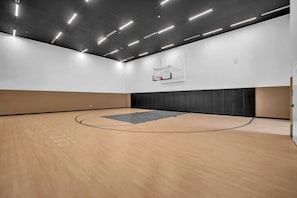 An indoor basketball court with a wooden floor, a basketball hoop, and a wall-mounted rack. - Brand New Building & Amazing Amenities (Miami)