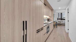 A modern kitchen with wooden cabinets, a built-in oven, and a dining area with a table and chairs. - Brand New Building & Amazing Amenities (Miami)