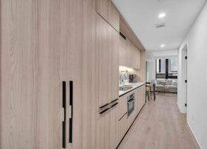 A modern kitchen with wooden cabinets, a built-in oven, and a dining area with a table and chairs. - Brand New Building & Amazing Amenities (Miami)