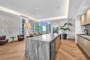 A modern kitchen with a marble island, wooden cabinets, and a large window offering a city view. - Stylish Bay View Studio w/Private Balcony/Downtown (Miami)