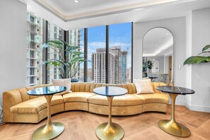 A modern living room with a curved sofa, two round tables, and large windows offering a city view. - Stylish Bay View Studio w/Private Balcony/Downtown (Miami)