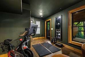 Ein Heimfitnessraum mit Trainingsgeräten, darunter ein Ergometer, Gewichte und Matten.