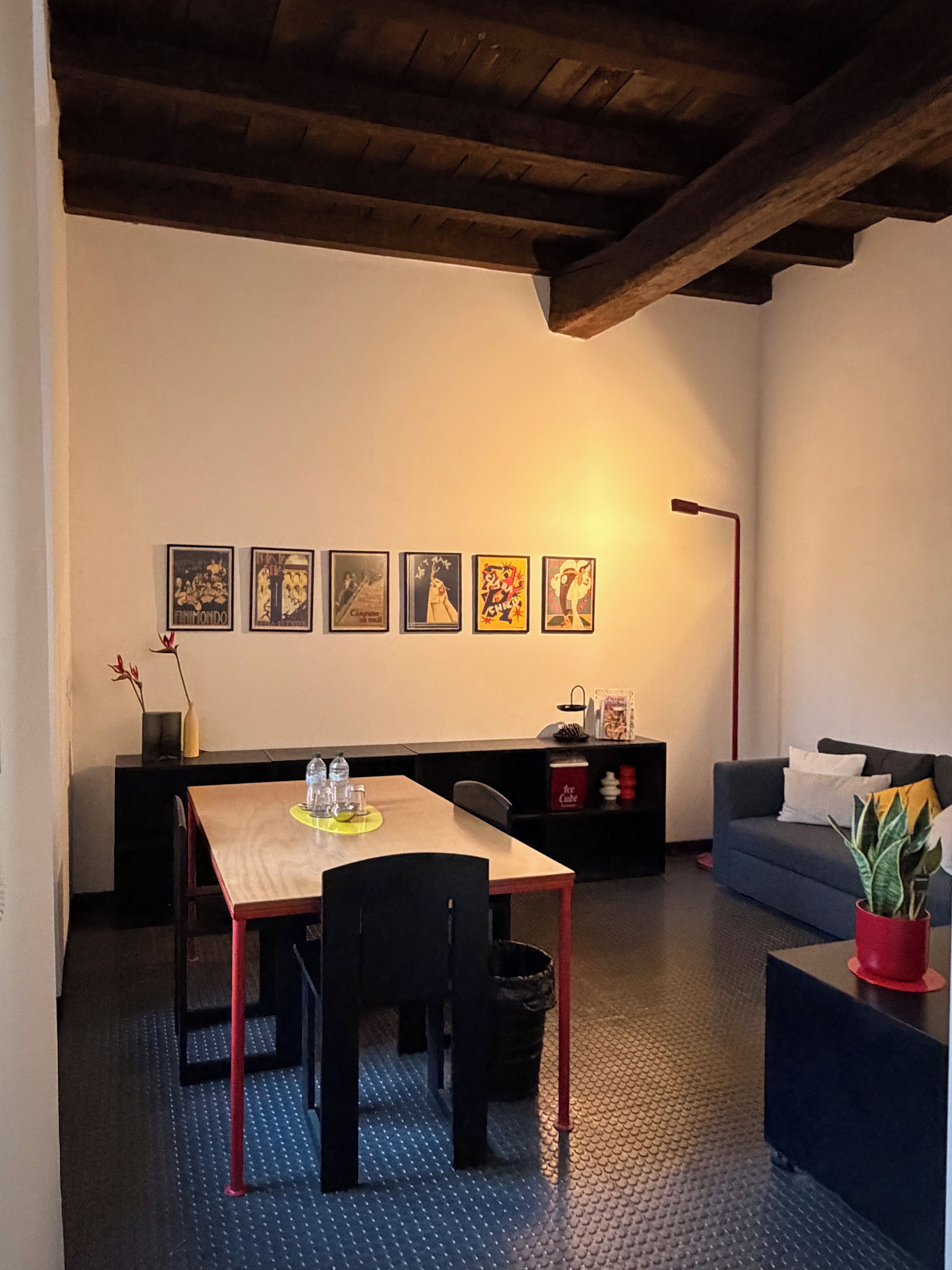 A room with a dining table, chairs, a sofa, a coffee table, a potted plant, and a wall with framed pictures.