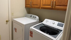 A laundry room with a front-loading washer and dryer, wooden cabinets above, and a door with a doorknob. - Charming 3-bedroom house in peaceful Stillwater with AC (Stillwater)