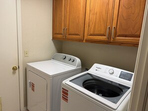 A laundry room with a front-loading washer and dryer, wooden cabinets above, and a door with a doorknob. - Charming 3-bedroom house in peaceful Stillwater with AC (Stillwater)