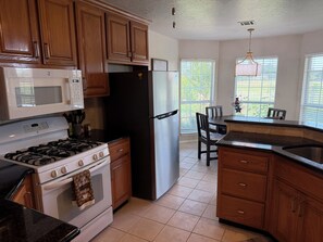 A kitchen with wooden cabinets, a stove, a refrigerator, and a dining area with chairs. - Charming 3-bedroom house in peaceful Stillwater, Oklahoma (Stillwater)