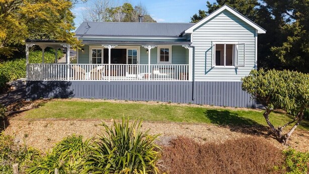 A single-story house with a porch, a fenced yard, and a clear sky.