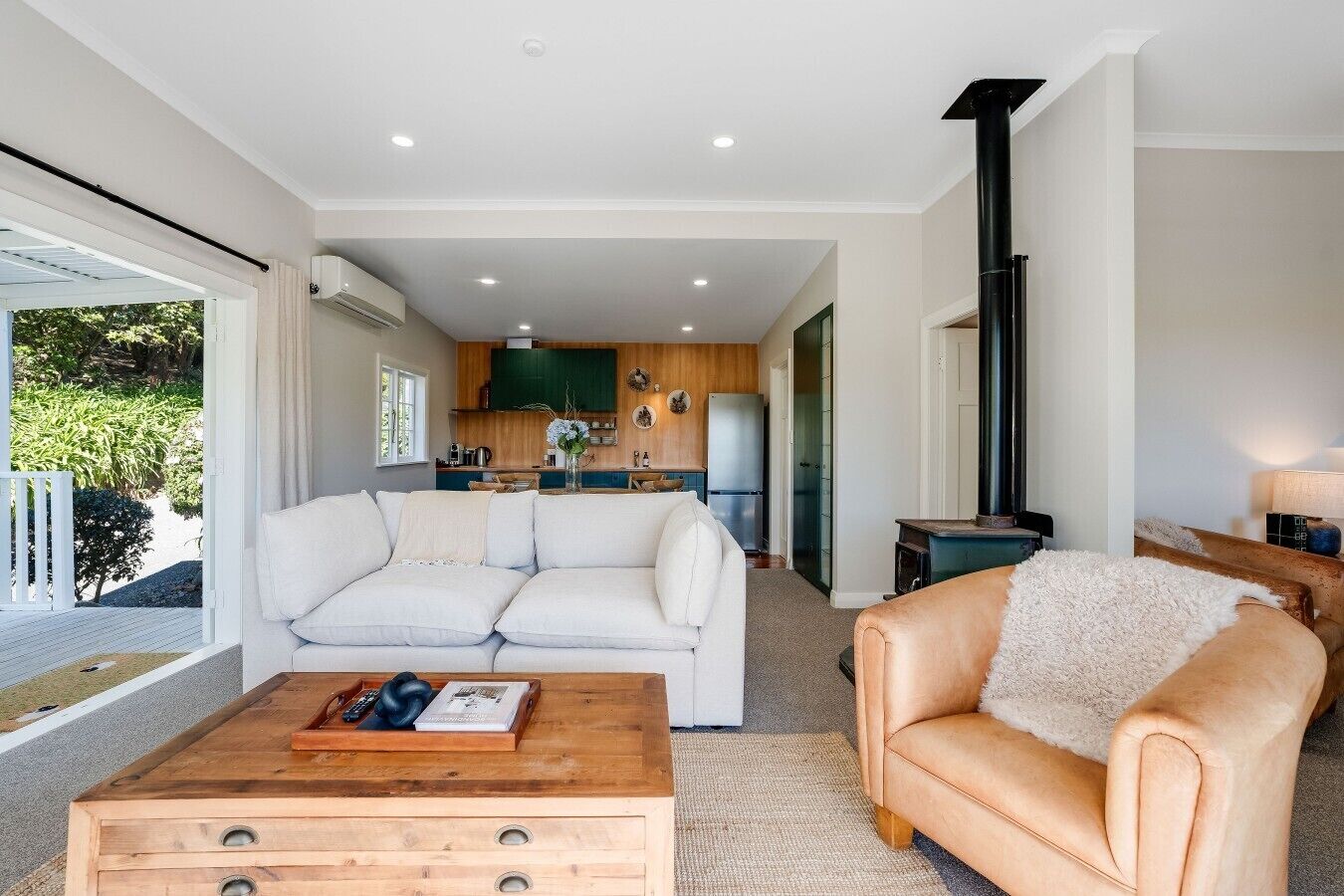A modern living room with a sofa, a coffee table, and a leather armchair. A kitchen is visible in the background with a stove and cabinets.