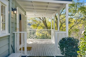 A covered porch with a white railing, a wooden floor, and a view of trees and hills in the background.
