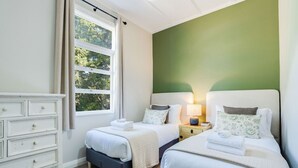 A bedroom with two beds, a dresser, and a window with curtains.