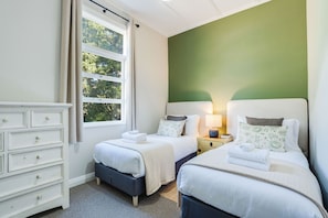 A bedroom with two beds, a dresser, and a window with curtains.