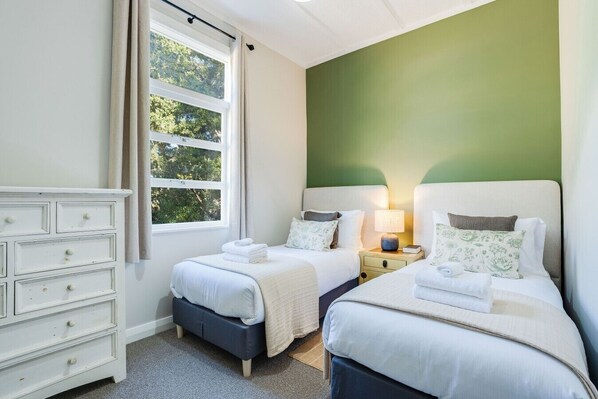 A bedroom with two beds, a dresser, and a window with curtains.