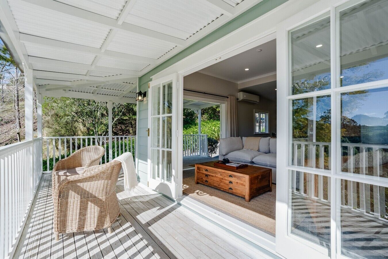 A covered porch with wicker furniture, a wooden coffee table, and a sofa.