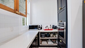 A modern kitchen with white tiles, a microwave, a coffee maker, and a built-in oven.