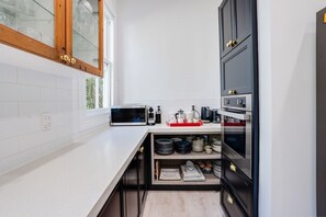 A modern kitchen with white tiles, a microwave, a coffee maker, and a built-in oven.
