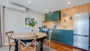 A modern kitchen with teal cabinets, a stainless steel refrigerator, and a dining area with a round table and chairs.