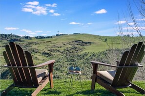 Dos sillas Adirondack mirando un paisaje con colinas ondulantes y cielo despejado.