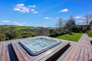 Ein Whirlpool auf einer Holzterrasse mit Blick auf eine grüne Landschaft und Bäume.