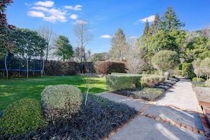Ein gepflegter Garten mit einem gepflasterten Weg, ordentlich geschnittenen Hecken und verschiedenen Bäumen.