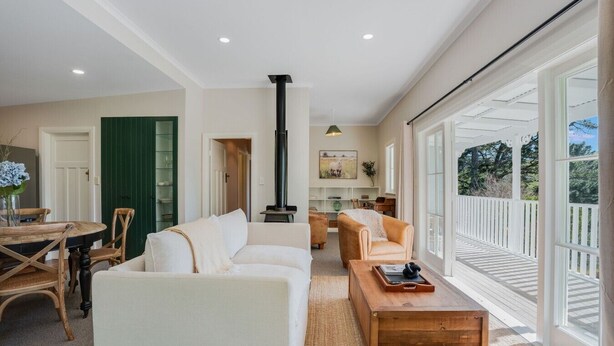 A spacious living room with a fireplace, a dining area with a round table and chairs, and large windows offering a view of the outdoors.