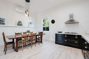 Eine moderne Küche mit Essbereich, ausgestattet mit einem Holztisch und Stühlen, einem schwarzen Schrank mit goldenen Griffen und einer Edelstahl-Dunstabzugshaube.
