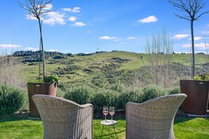 A terrace with wicker chairs, a small table, and two wine glasses.