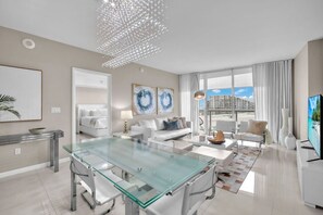 A modern living room with a glass-top dining table, white sofas, and a large window offering a city view. - The Enso Suite Luxury Brickell (Miami)