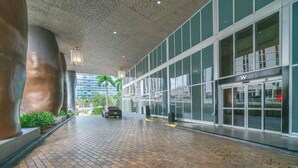 Entrada de un edificio moderno con un camino empedrado de ladrillo, grandes ventanales de vidrio y un coche estacionado en el interior.
