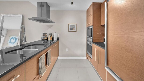Una cocina moderna con un lavamanos de acero inoxidable, armarios de madera, horno empotrado y una lámpara colgante.