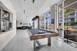 A modern pool table in a spacious room with a large window, a seating area, and a television. - New Modern 2BR/2BA Design District + Free Parking (Miami)