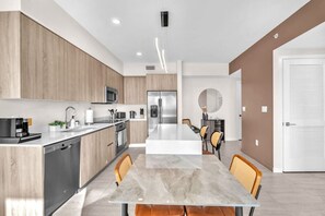 A modern kitchen with a central island, stainless steel appliances, and a dining area with a marble table. - New Modern 2BR/2BA Design District + Free Parking (Miami)