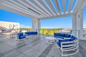 Um terraço no telhado com design moderno, apresentando uma pérgula branca, um conjunto de sofá azul e uma pequena mesa redonda.