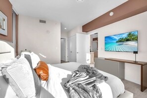 Quarto de hotel com uma cama, televisão de tela plana e vista para a praia pela janela.