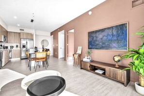 Uma cozinha moderna com eletrodomésticos de aço inoxidável, uma sala de jantar com mesa e cadeiras redondas, e uma sala de estar com uma pintura grande e um globo sobre um aparador.