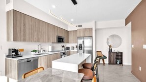 A modern kitchen with a central island, stainless steel appliances, and a dining area with a marble table. - New Modern 2BR/2BA Design District + Free Parking (Miami)