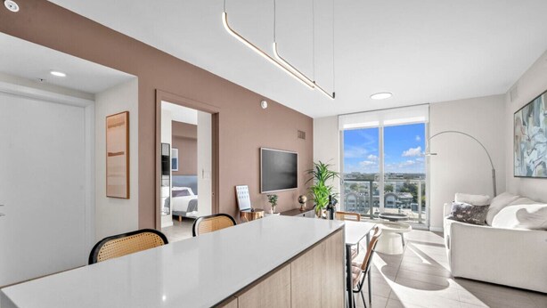 A modern living space with a central island dining table, a sofa, and a television. - New Modern 2BR/2BA Design District + Free Parking (Miami)