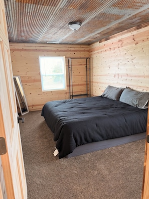 Une chambre avec un lit, une fenêtre et une échelle métallique adossée au mur.