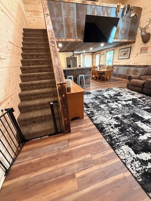 Un intérieur en bois avec un escalier recouvert de moquette, un coin repas et un salon agrémenté d’un tapis à motifs.