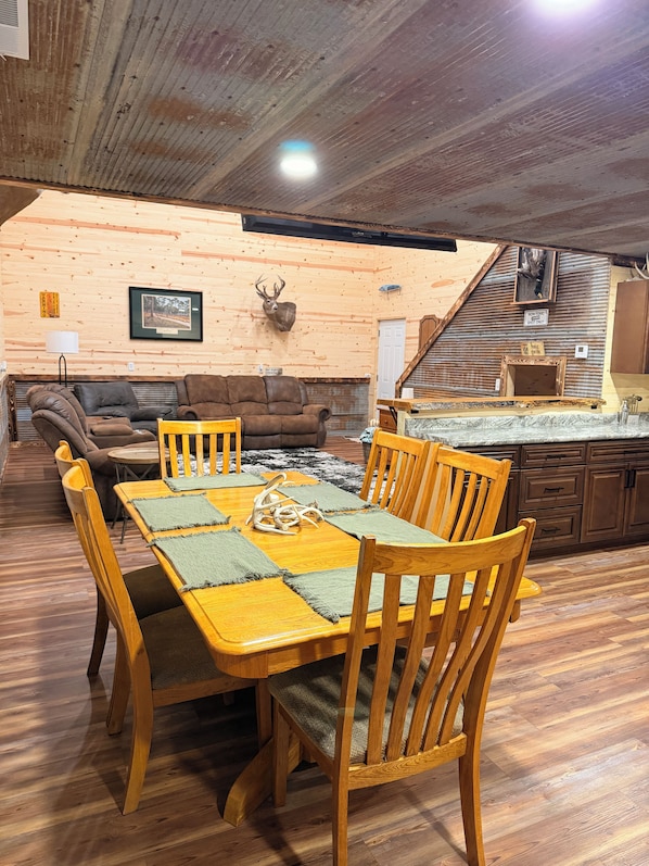 Un coin repas avec une table et des chaises en bois, une tête de cerf accrochée au mur, et un espace cuisine avec des placards en bois.