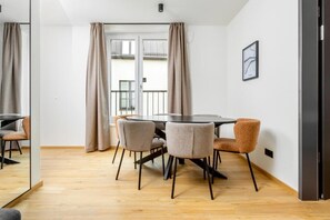 Un comedor con una mesa redonda y sillas, vistas a un balcón a través de un ventanal, y un cuadro en la pared.