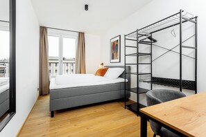 A compact hotel room with a bed, a desk, a chair, a wardrobe, and a window with curtains.