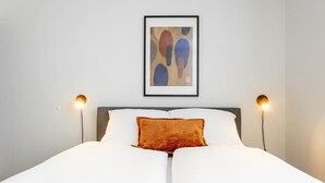 A bed with white bedding, a brown accent pillow, and two bedside lamps.