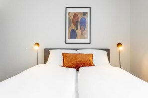 Un lit avec une literie blanche, un coussin décoratif marron et deux lampes de chevet.