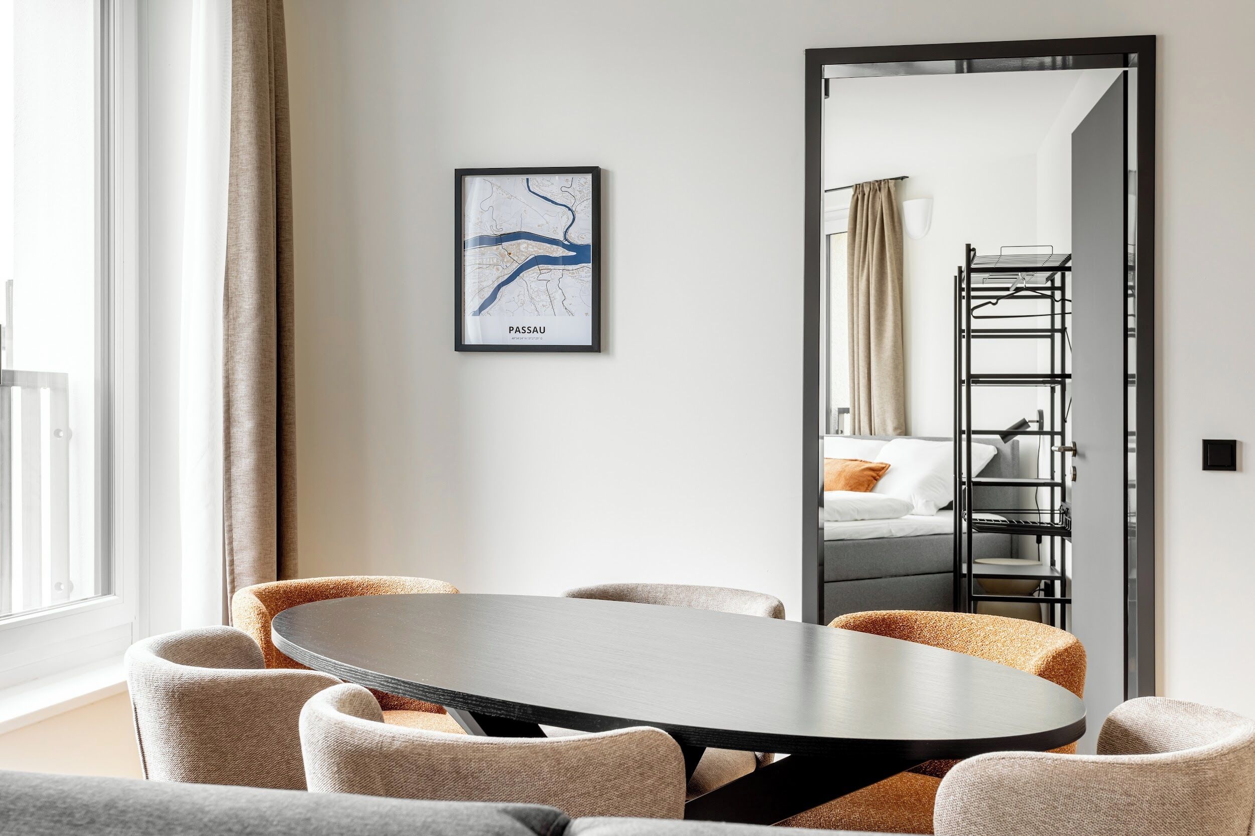 Een moderne hotelkamer met een ronde eettafel, comfortabele zitplaatsen, een grote spiegel en een ingelijste kaart aan de muur.