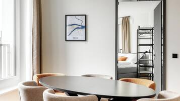 Een moderne hotelkamer met een ronde eettafel, comfortabele zitplaatsen, een grote spiegel en een ingelijste kaart aan de muur.