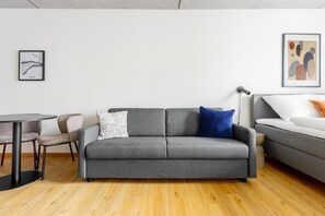 Un salon moderne avec un canapé gris, un divan blanc, une table ronde et deux chaises.