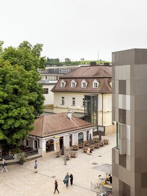 A courtyard with outdoor seating, a building with a tiled roof, and a large tree.