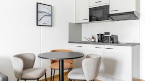 A modern kitchen with white cabinetry, a black microwave, and a coffee machine. There is a framed map on the wall and two chairs around a small table.