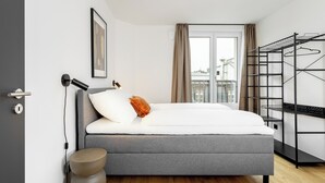 A modern bedroom with a grey sofa bed, a bedside lamp, a framed picture, and a metal drying rack.