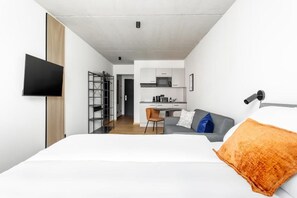 Una habitación de hotel moderna con cama, televisión, kitchenette y zona de estar.